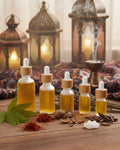 Five dropper bottles with a yellow liquid on a wooden surface with incense and lanterns in the background.